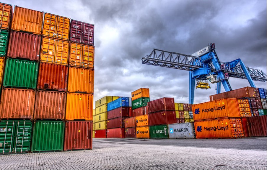 Stacked Hapag-Lloyd, MAERSK and UASC shipping containers at a Green Freeport with a quayside gantry crane